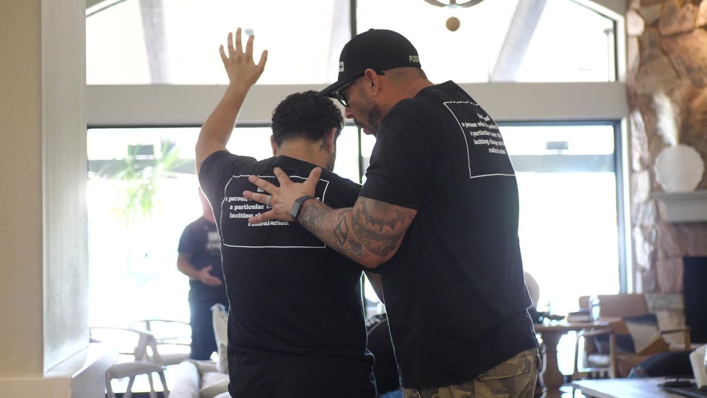 A man in a Firebrand shirt praying over another man at the Firebrand Intensive
